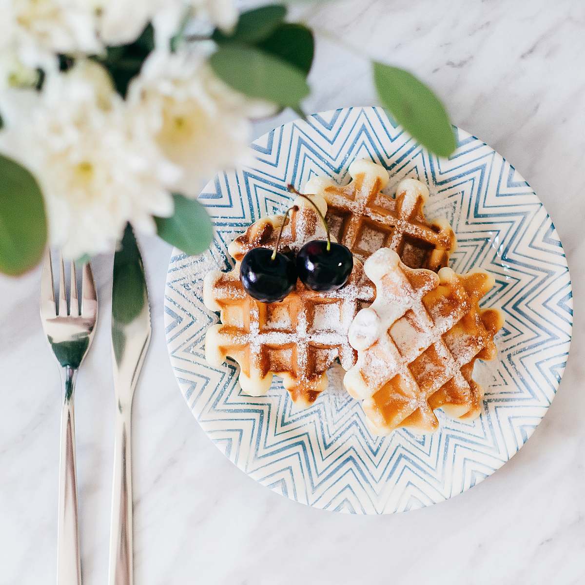 waffle 3 waffles on saucer with 2 cherry fruits beside fork and bread knife fresh