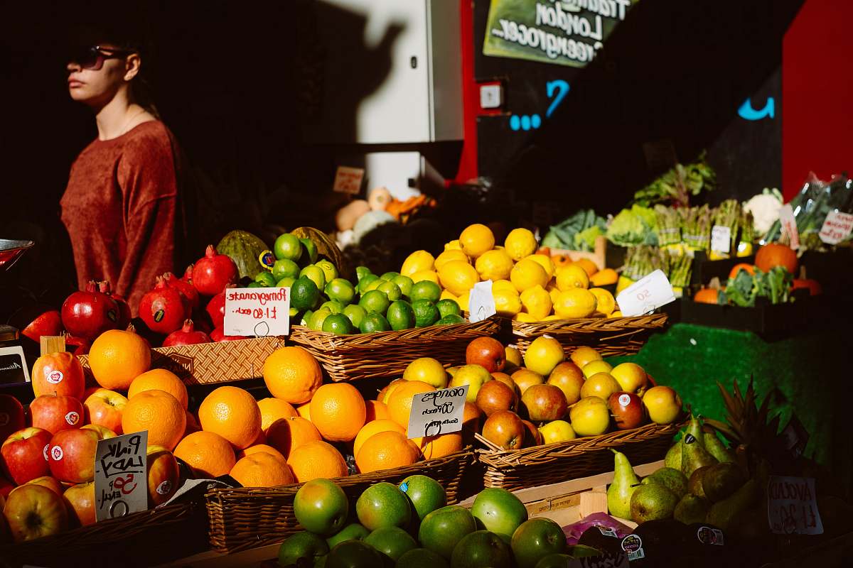 fruit assorted fruits on fruitstand beside woman in brown top citrus fruit
