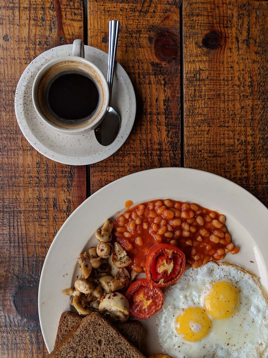 egg black coffee near sunny side up egg with sliced tomatoes, mushroom and bread on plate breakfast