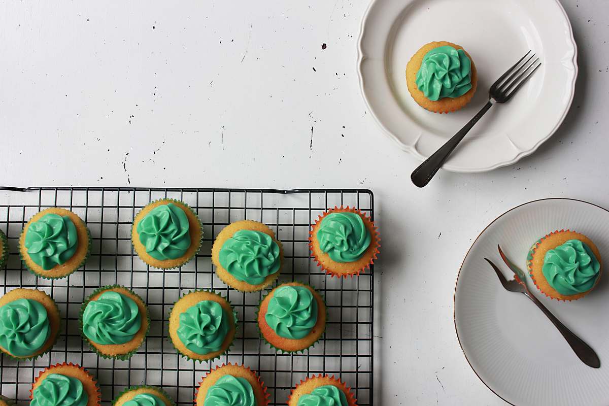 creme cupcakes with green toppings and two plate with one cupcake on top with fork on side icing