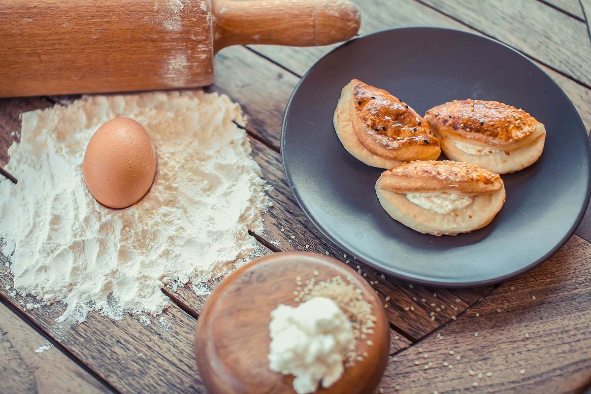 egg egg on top of dough beside round gray ceramic plate with buns on top tool