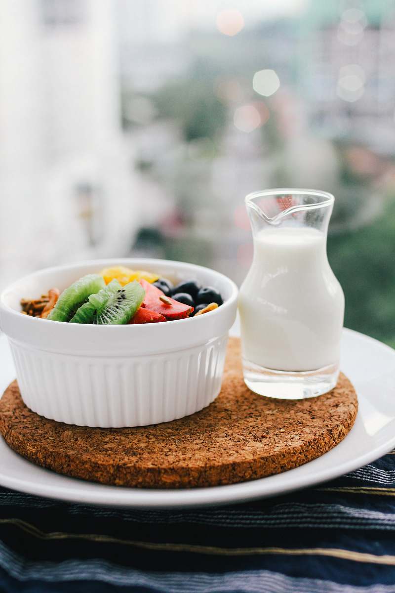 healthy fruit salad inside bowl beside glass of milk on brown board bowl