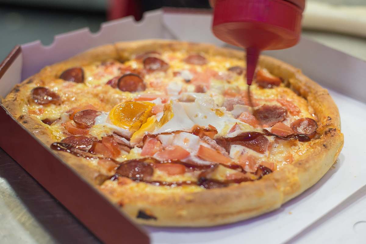 dish ketchup being poured on pizza pizza