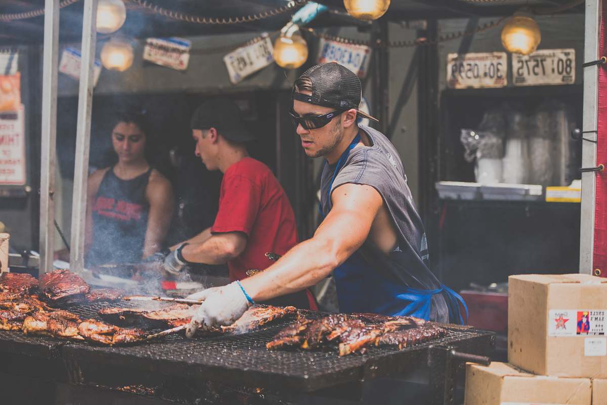bbq man standing infront of grill while holding tong person