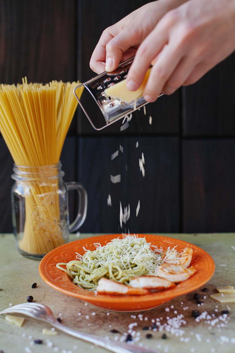 pasta person grates cheese on top of pasta noodle
