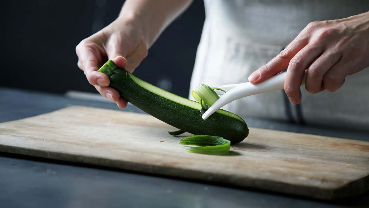 vegetable person pealing green cucumber inside room zucchini