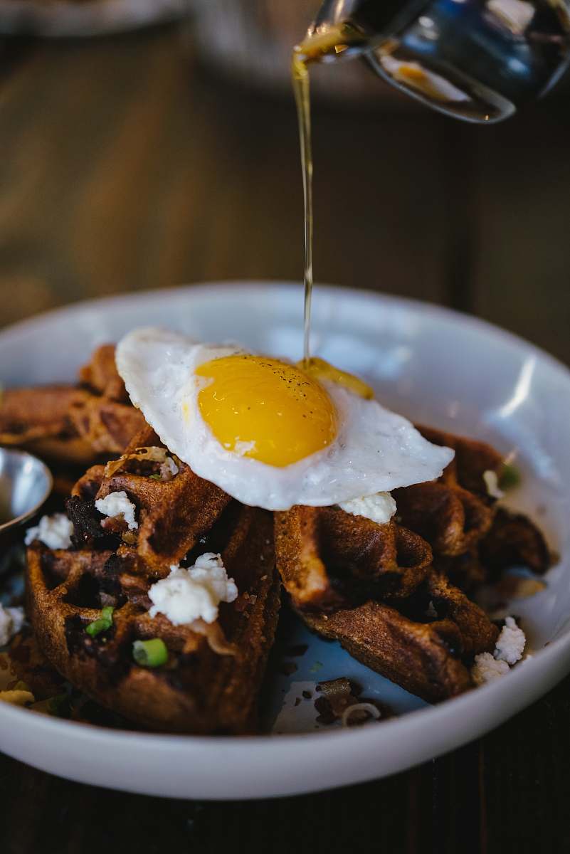 egg person pouring maple syrup on bowl of waffle with sunny side up egg bread