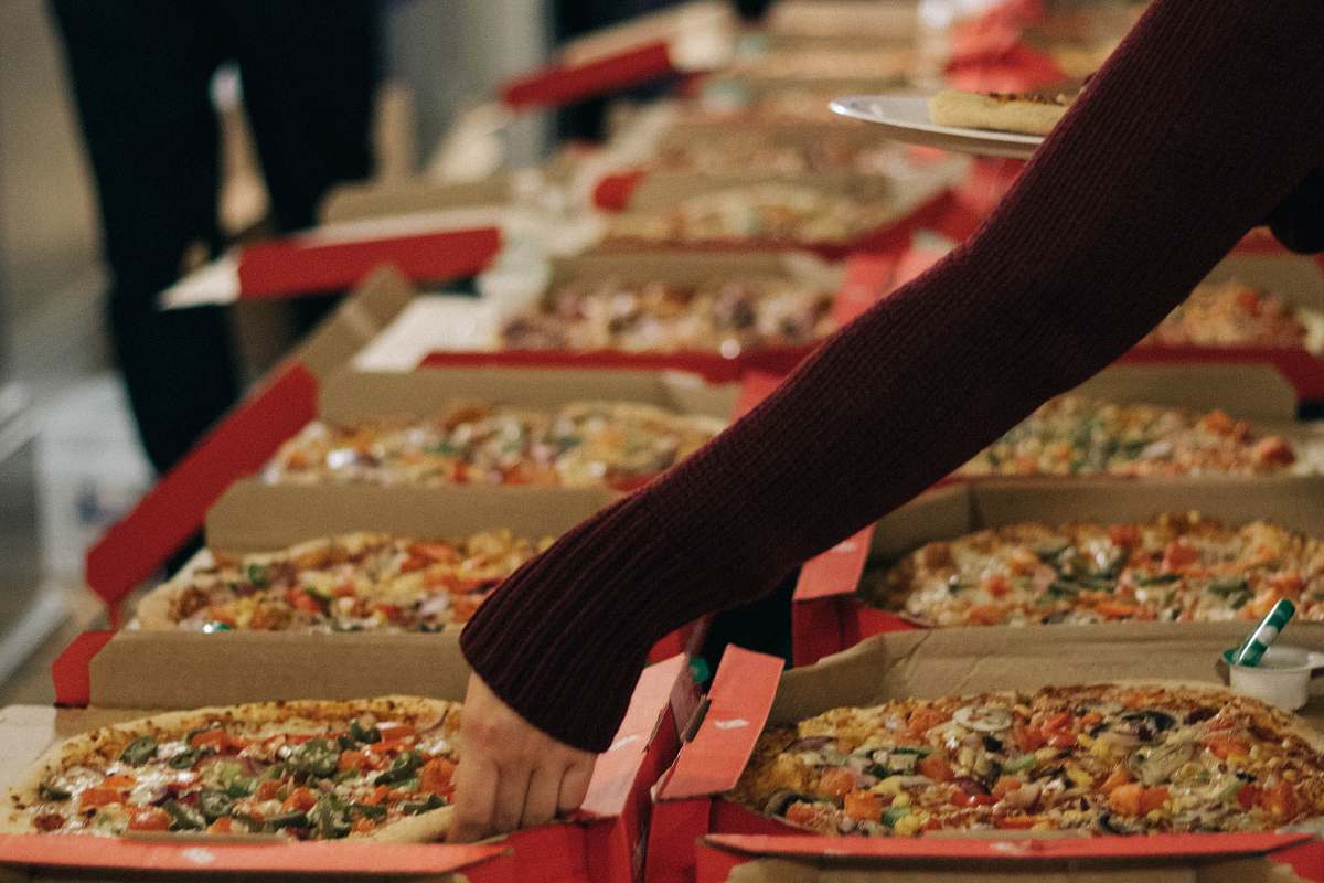 meal person reaching of a pizza on other side of table pizza