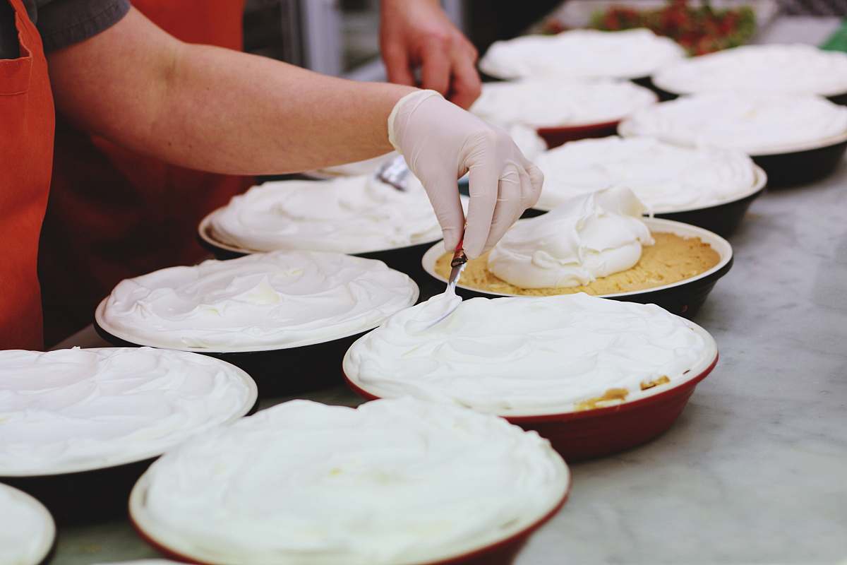 dessert person wearing white latex gloves putting cream on bowls cream