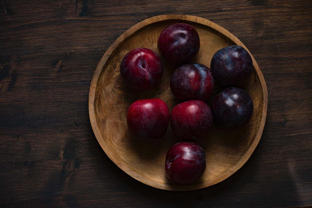 fruit red plum fruits on round brown wooden plate plum