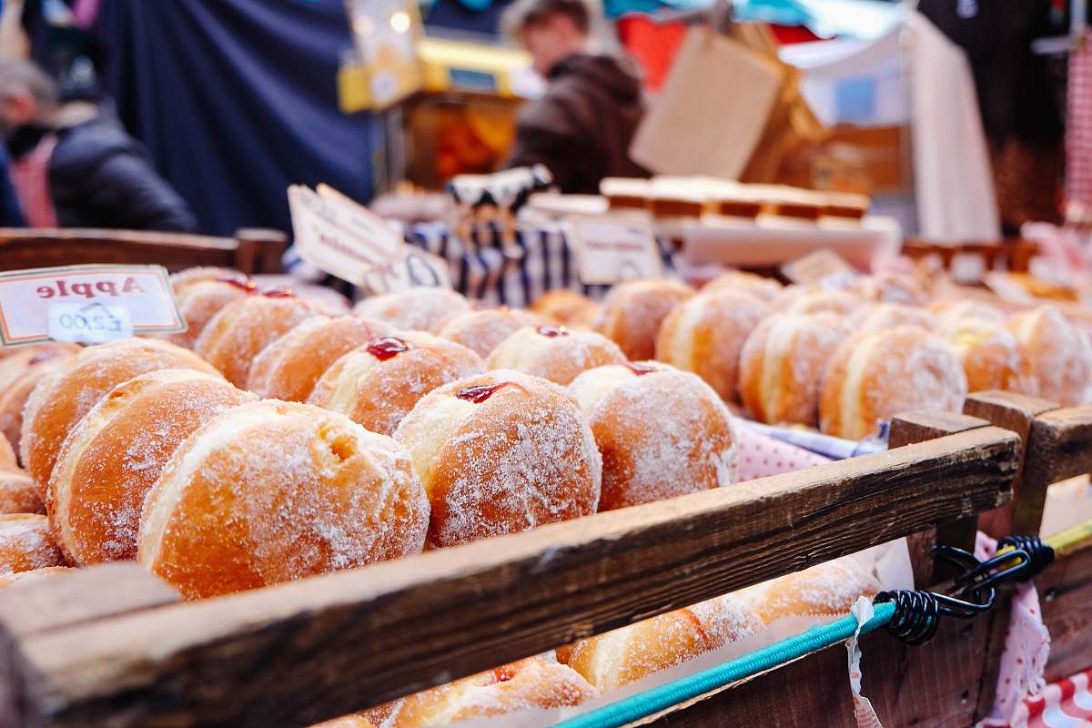 person selective focus photography of doughnuts display on brown wooden trays near person wearing black hoodie donut