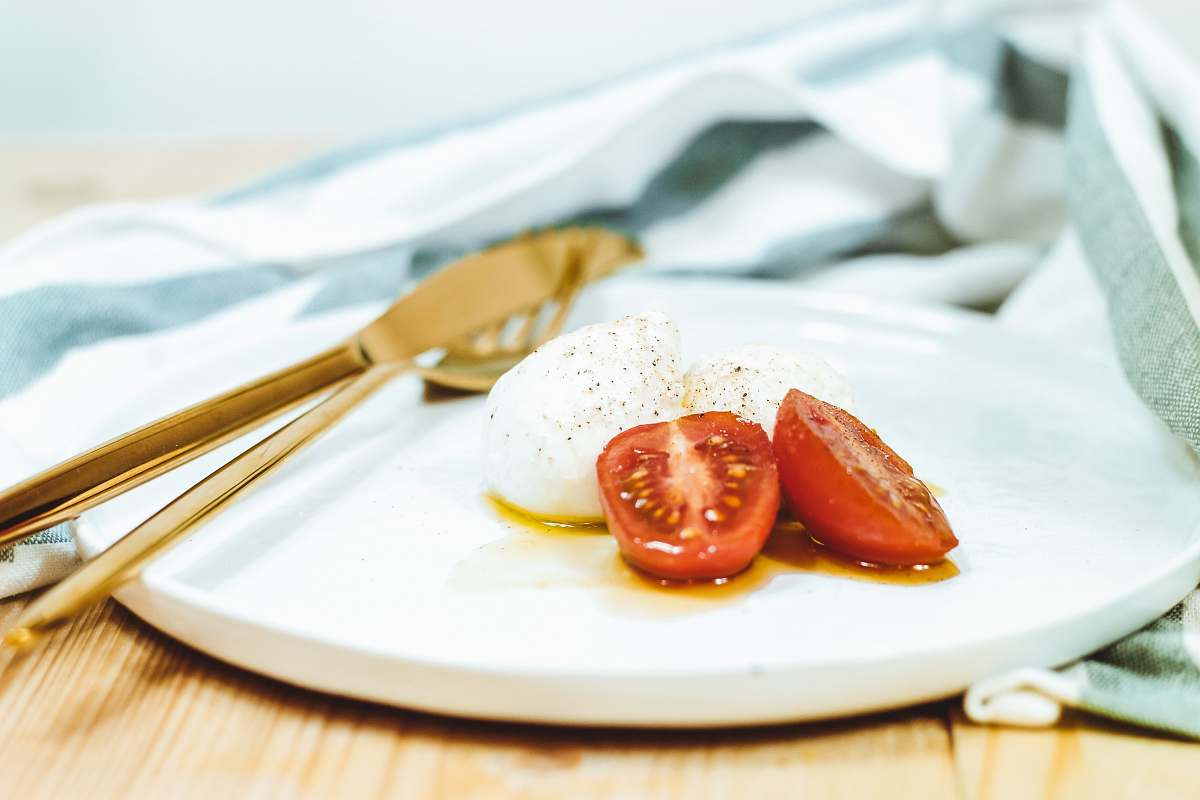 plate sliced tomato and mozzarella cheese on white plate beside brass-colored knife and fork tomato