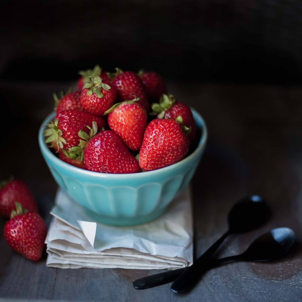 fruit strawberry fruit on blue ceramic bowl beside two black spoons strawberry