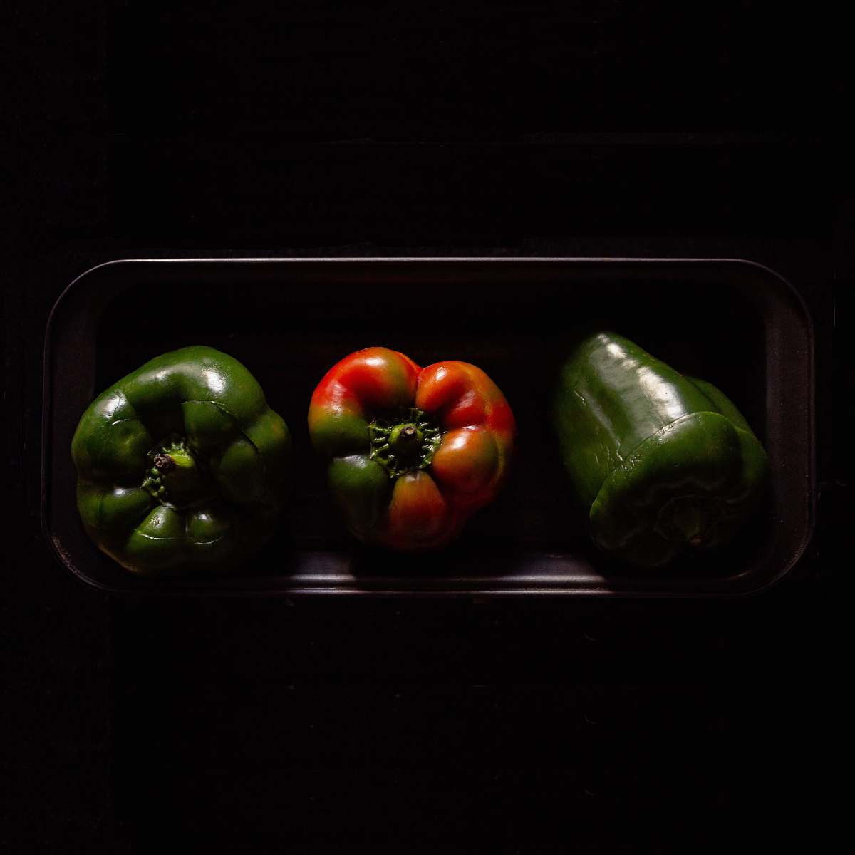 vegetable three orange and green bell peppers on black plate pepper