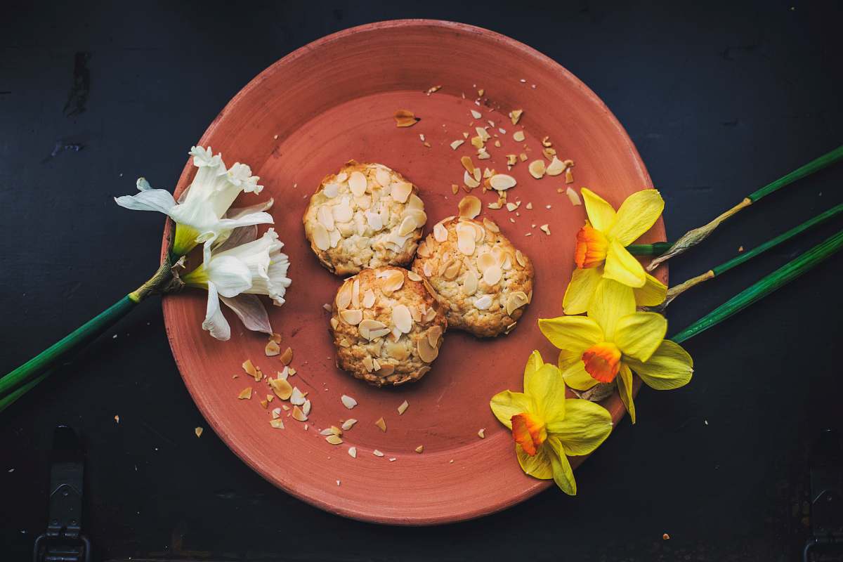 almond three round cookies on brown plate with petaled flowers flowers