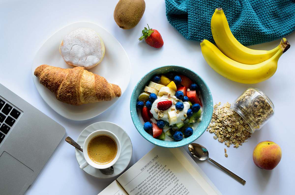 breakfast top view of strawberry and berries parfait in bowl near croissant and laptop meal
