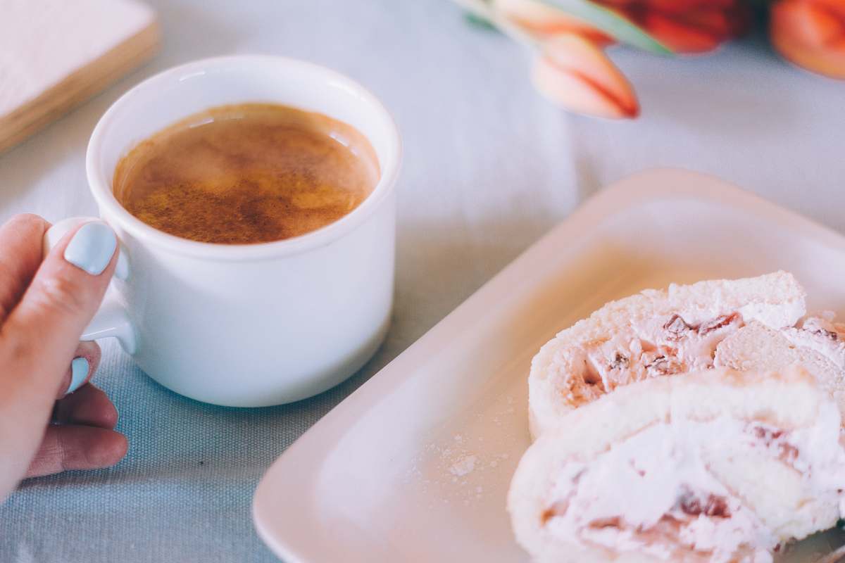 cream white mug filled with brown liquid beside tray with pastry creme