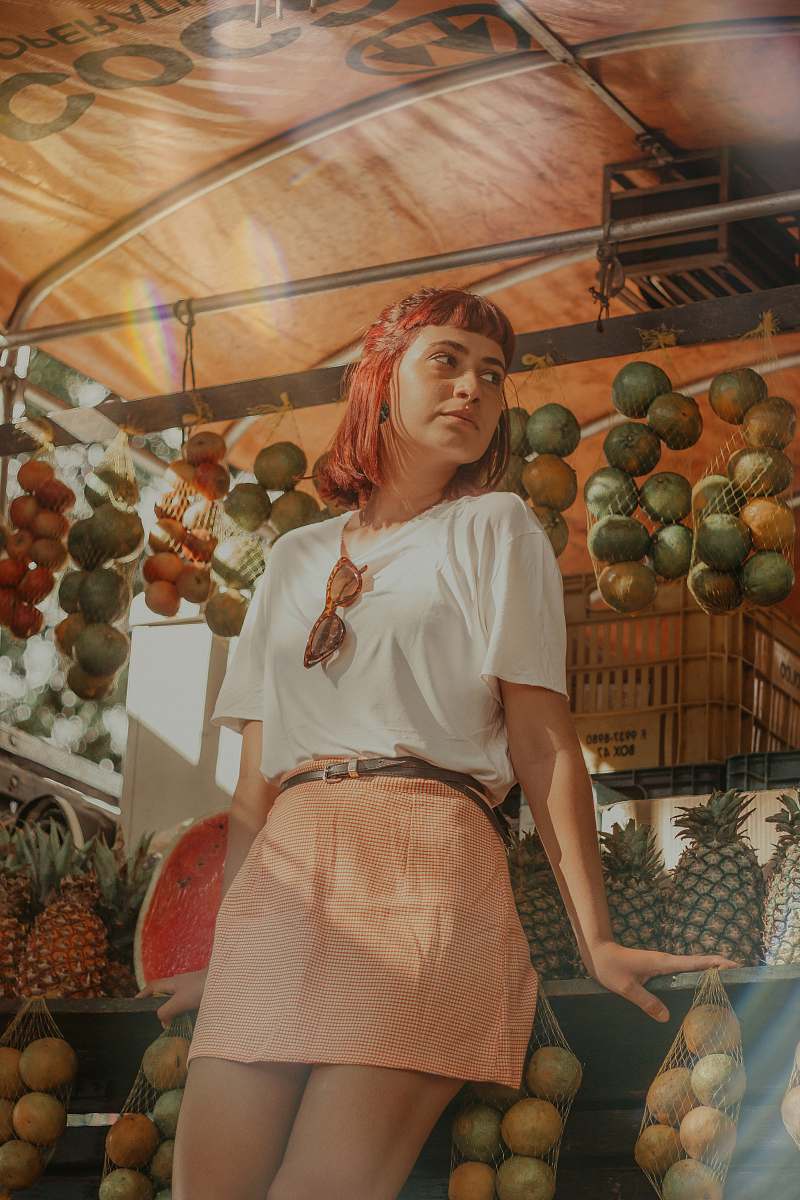 fruit woman in white shirt and pink mini skirt looking sideways plant