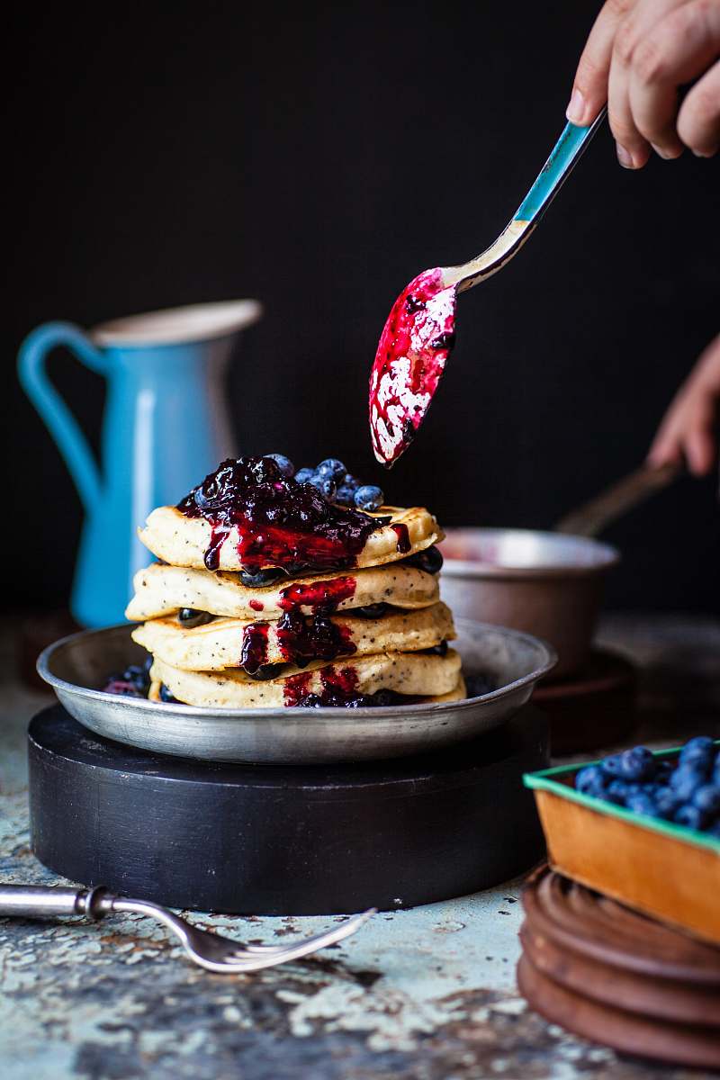 food person holds spoons with berries near waffles on plate blueberry