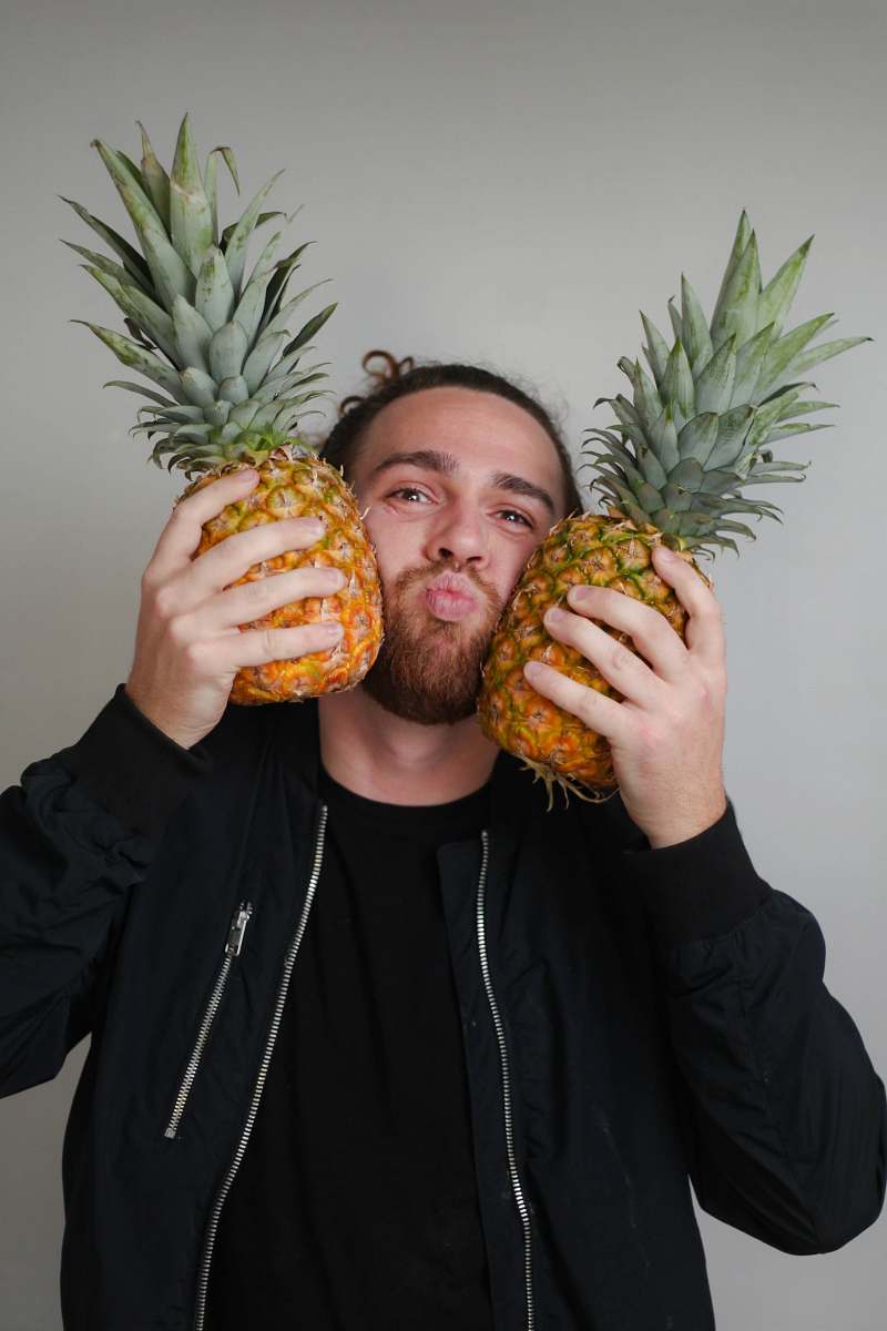 fruit man pressing both cheeks with pineapples with crown pineapple