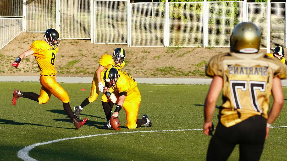 human football player about to kick a football held by another player during daytime person