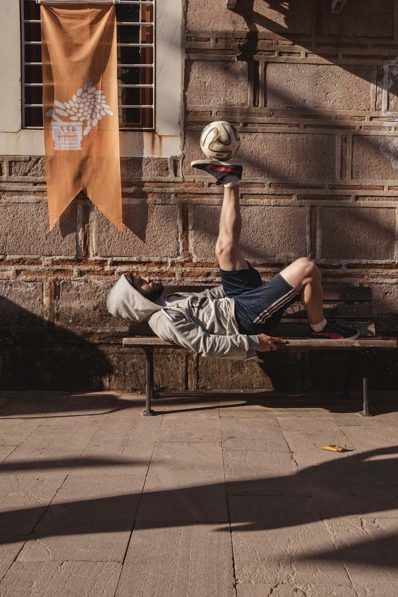 clothing man in gray hooded jacket and black shorts playing ball while lying on bench human