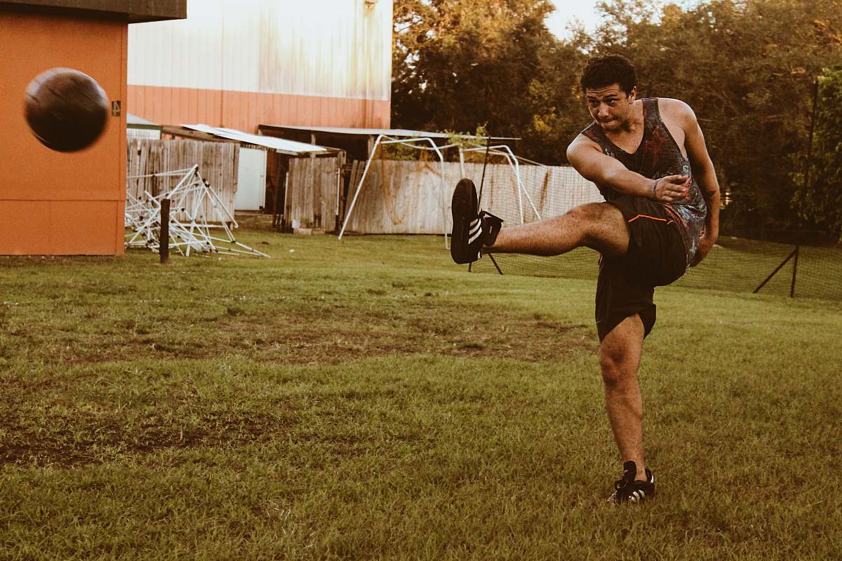 human man kicking brown soccer ball person