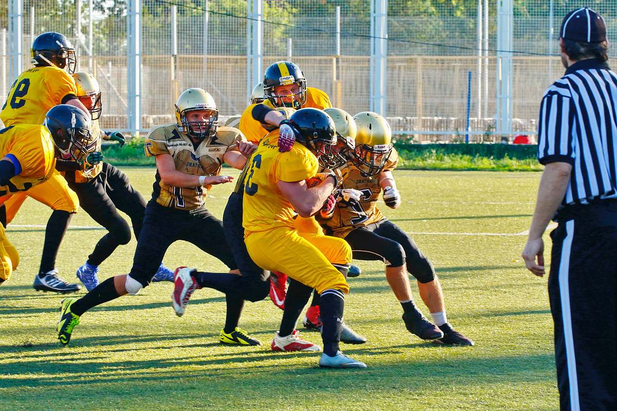 clothing people playing american football with referee on the field during daytime helmet