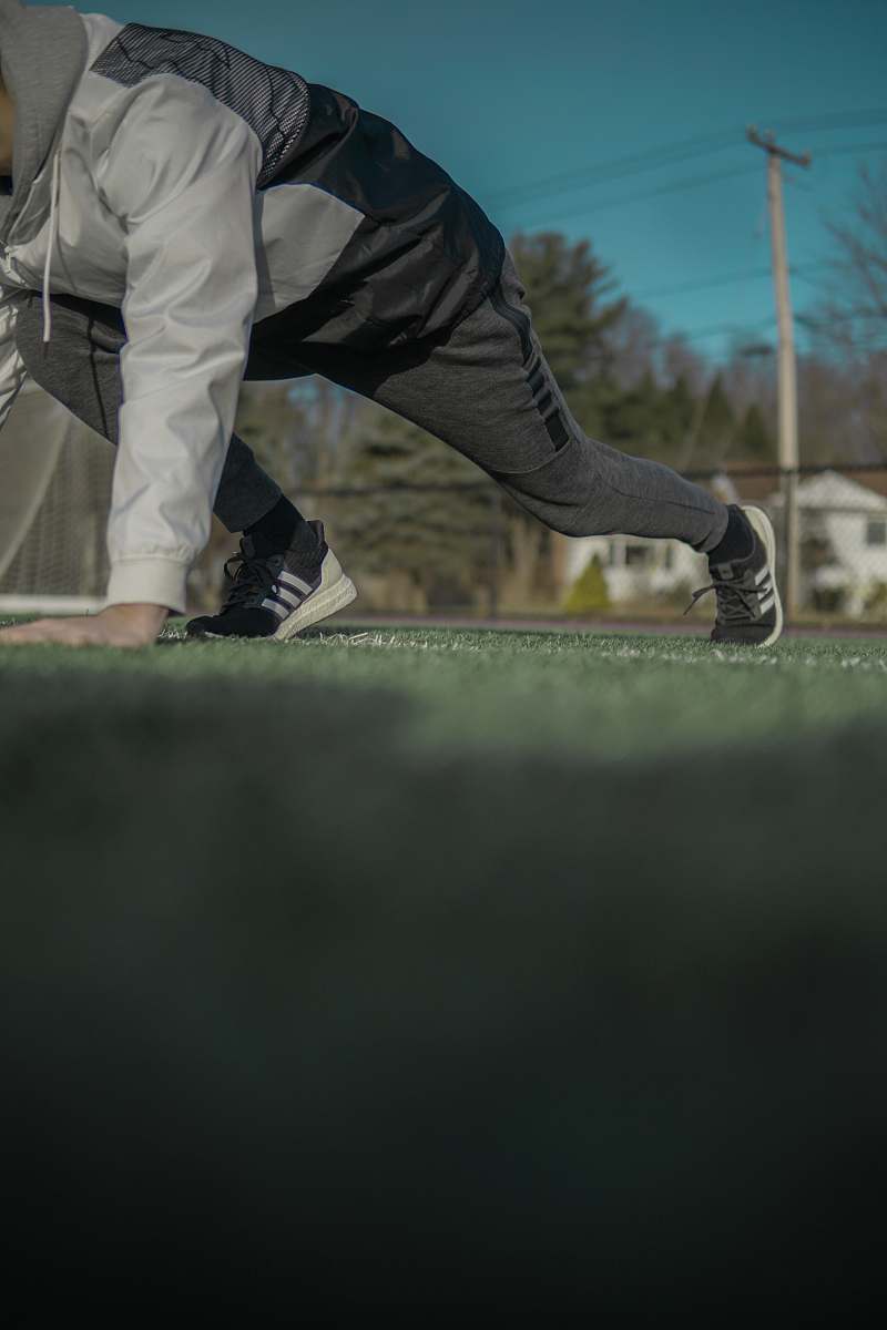 apparel man in grey track pants and jacket with hand on grass footwear