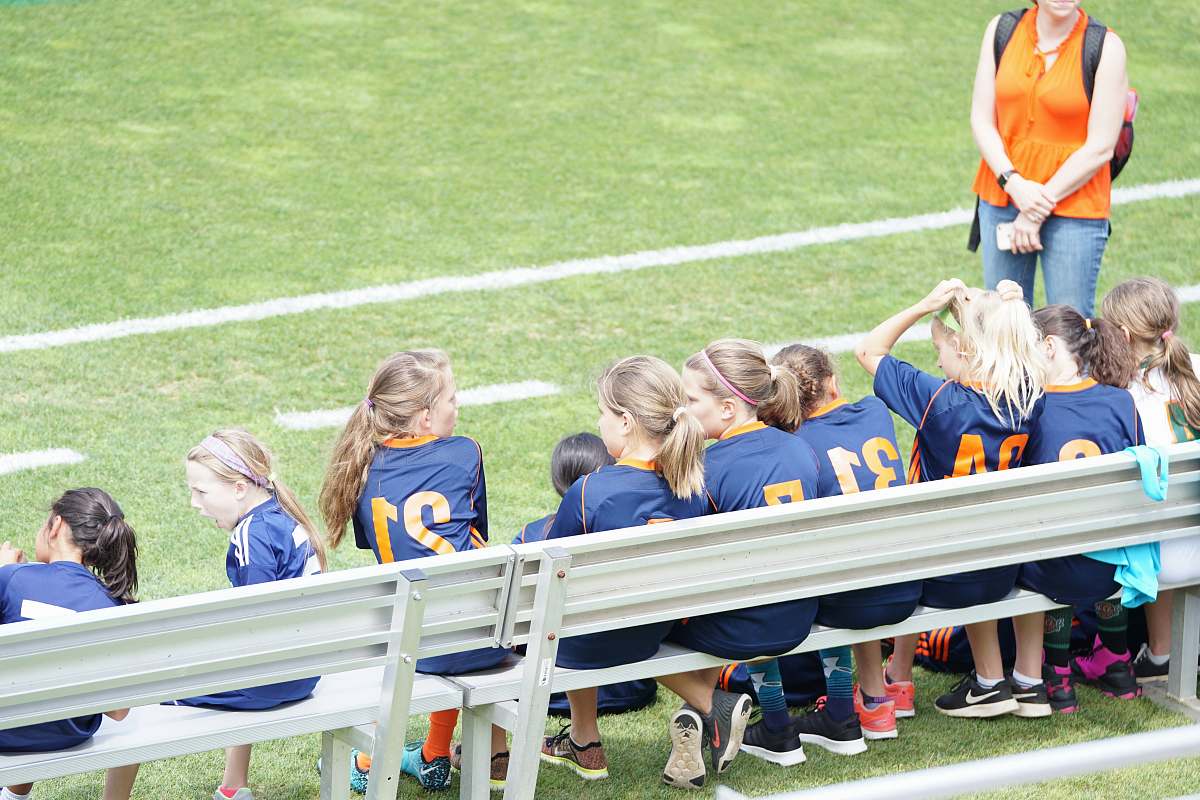person all girl football team sitting on white bench beside green field people