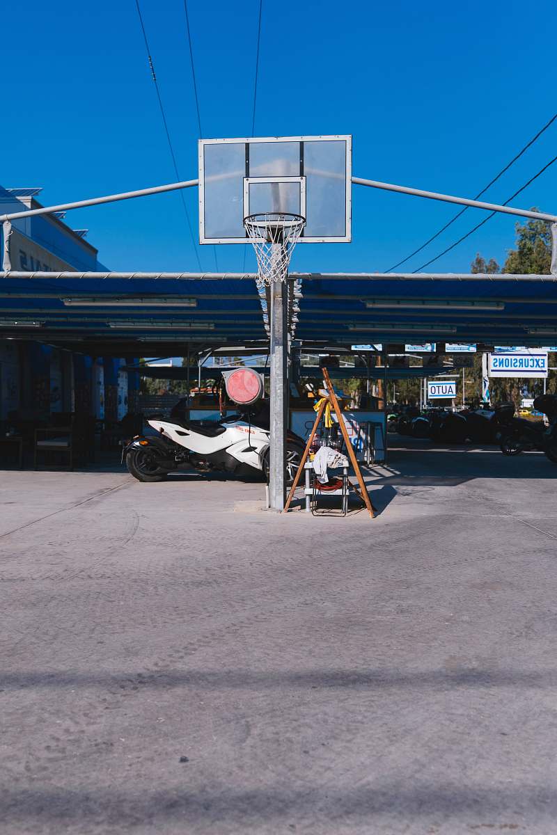people basketball system in front of white sports bike parked under blue roofed space during daytime person