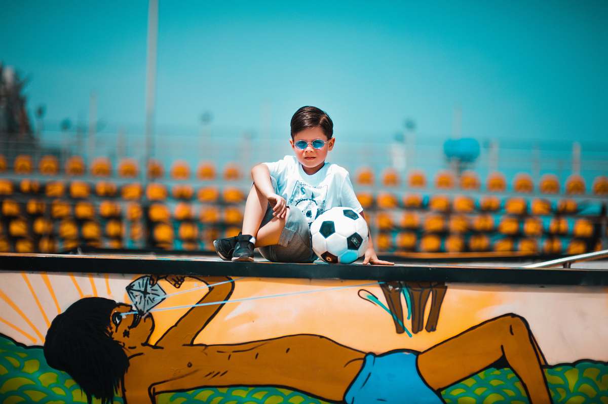 person boy sitting on graffiti wall beside soccer ball accessories