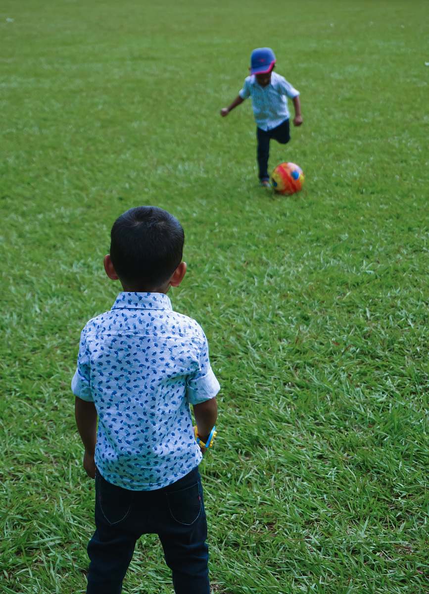 person child about to kick soccer ball and another boy standing people
