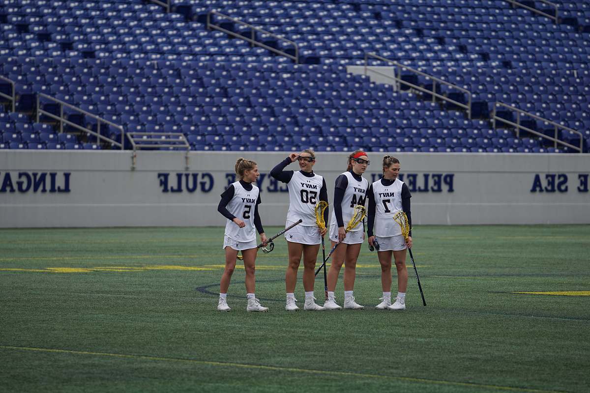 person four women holding lacrosse sticks on field during daytime field