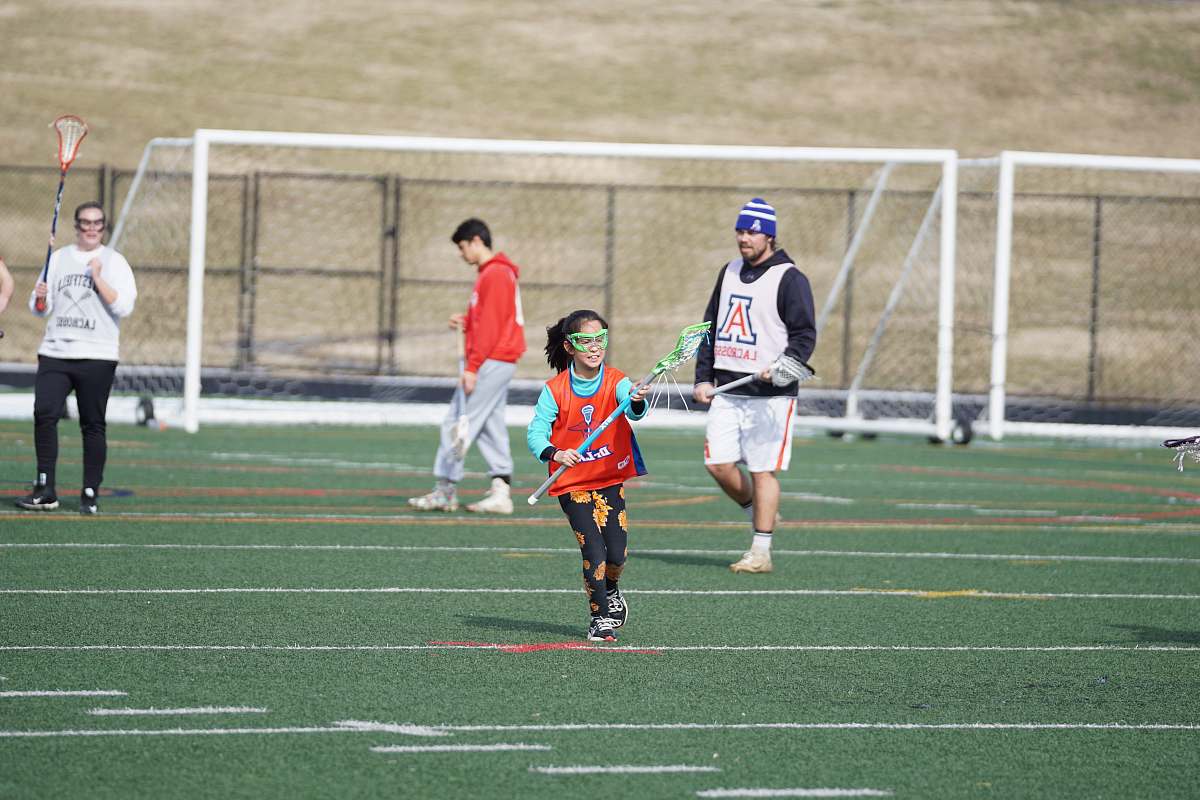 person girl in orange tank top playing lacrosse during daytime people