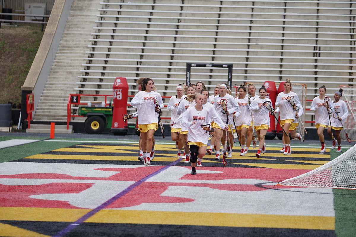 person girl's running on field holding lacrosse rackets people
