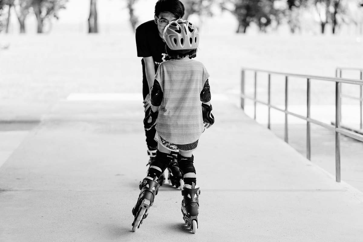 person grayscale photo of man and girl using inline skates near railings black-and-white