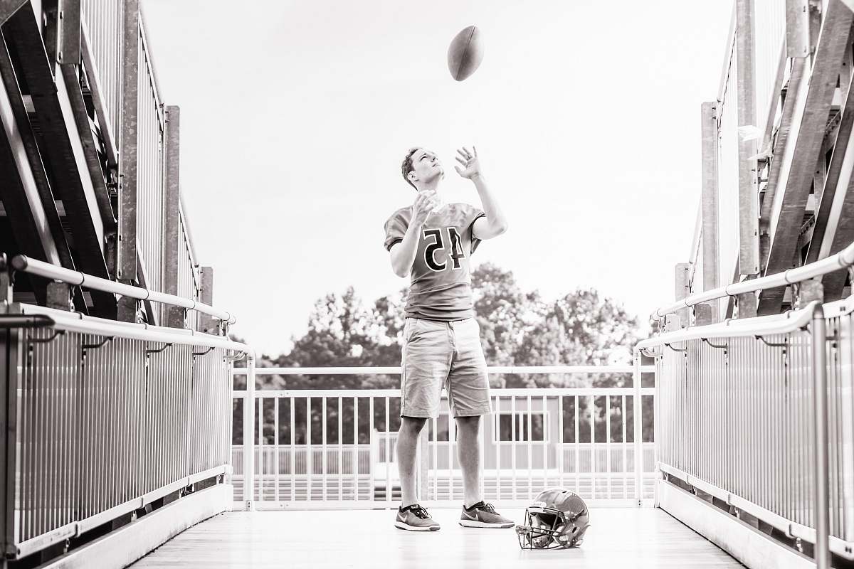 person grayscale photo of man standing while tossing football outdoors people