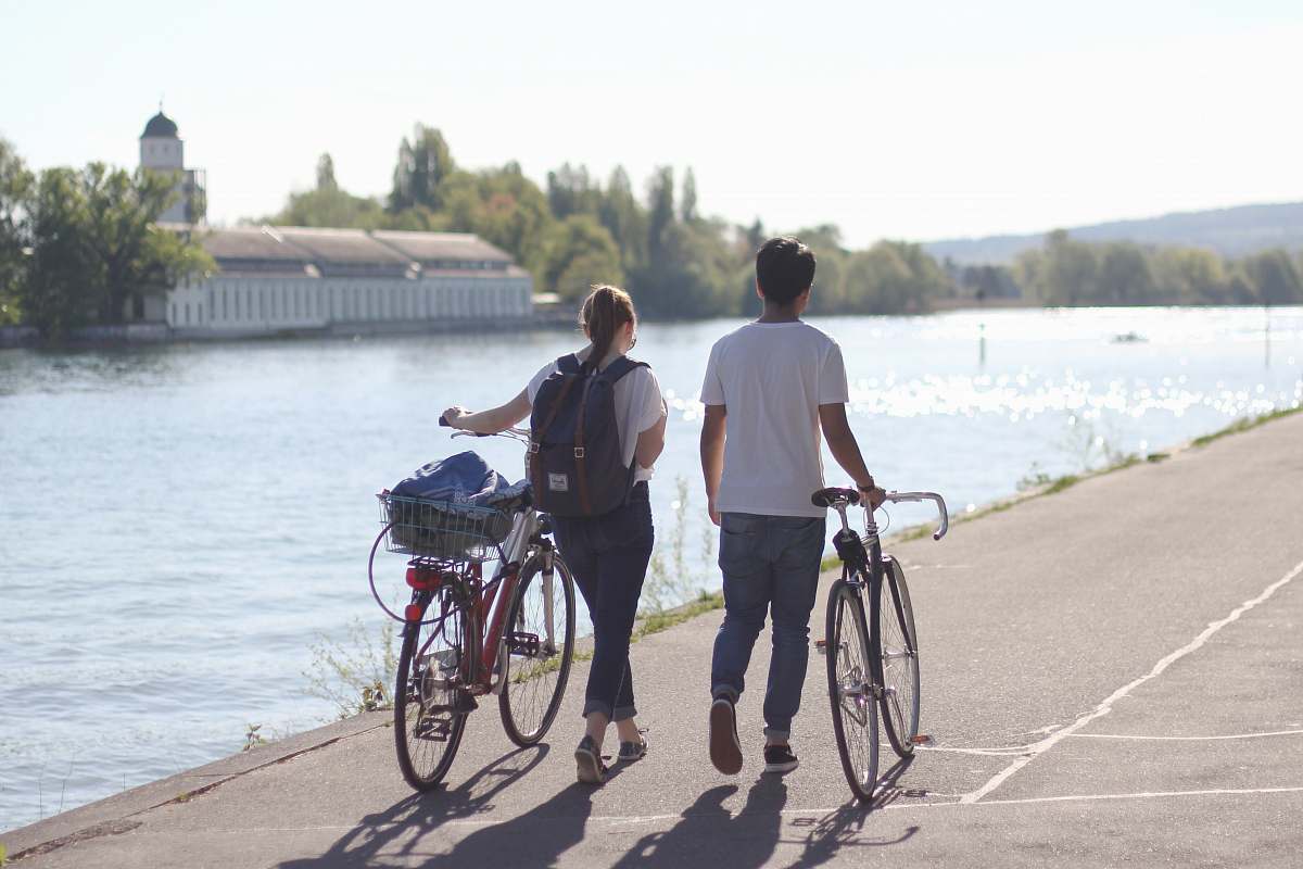 person man and women walking holding their bicycles beside body of water people