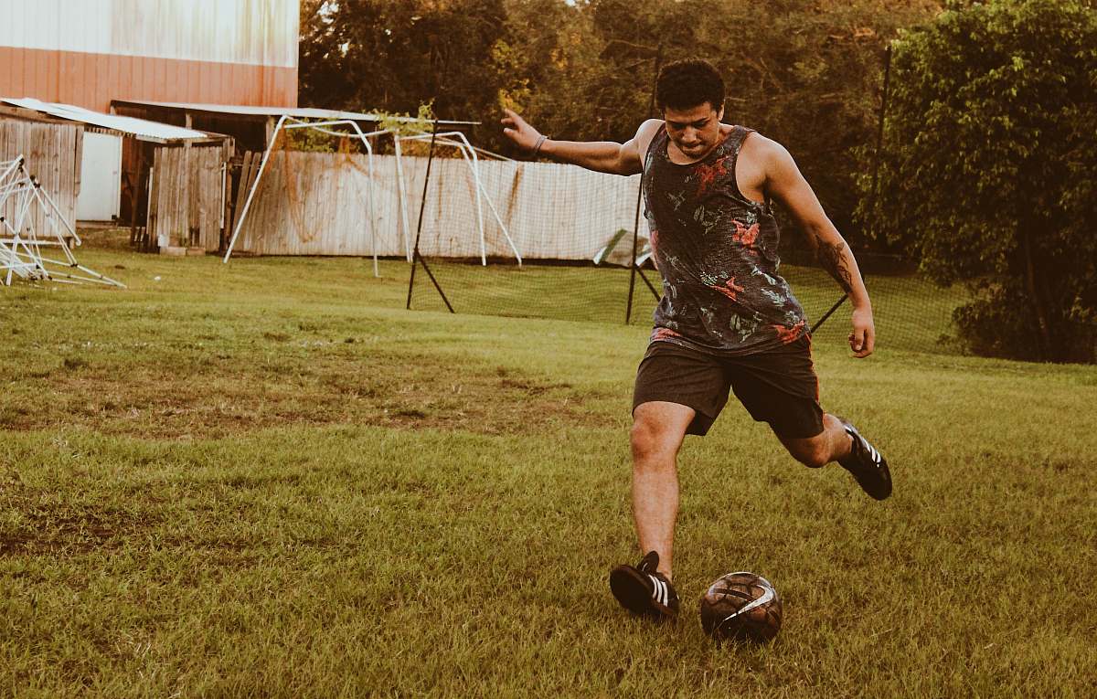person man kicking football on grass field during daytime apparel