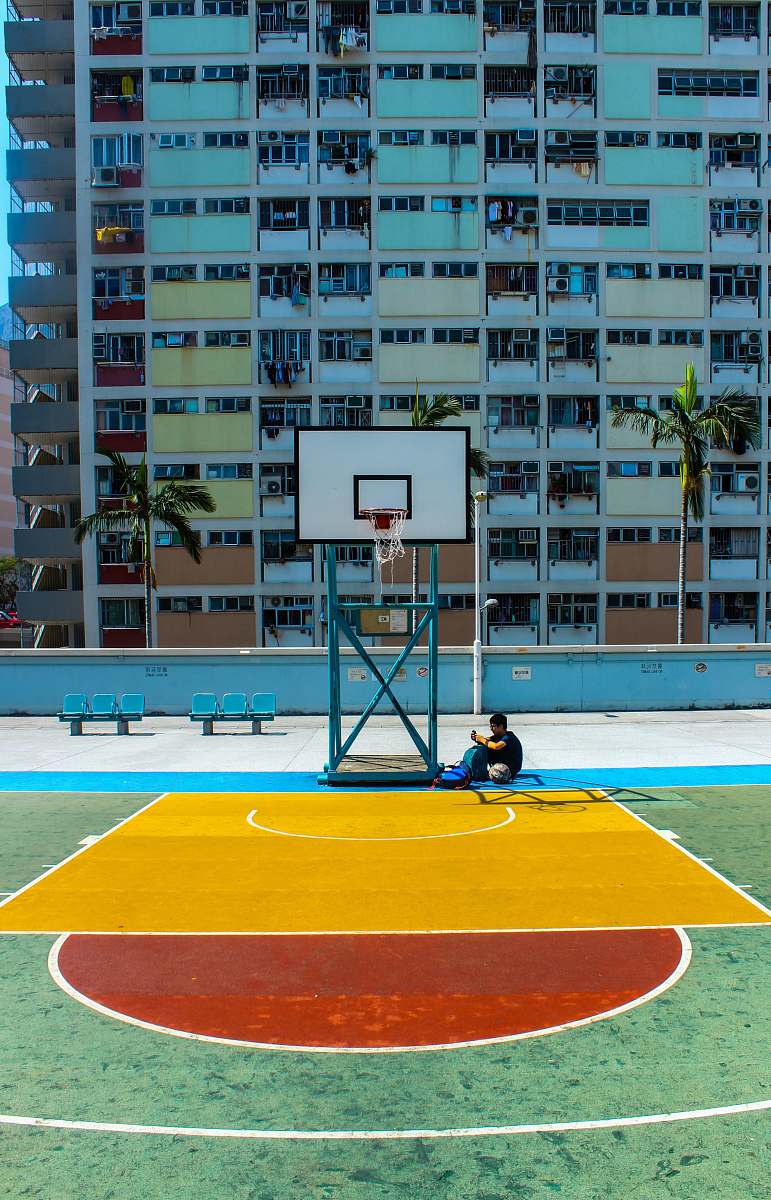 people man sitting below basketball hoop near the building during daytime person