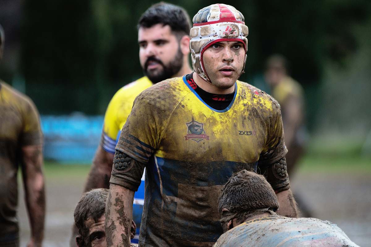 person man wearing yellow and blue shirt on mud field during daytime people