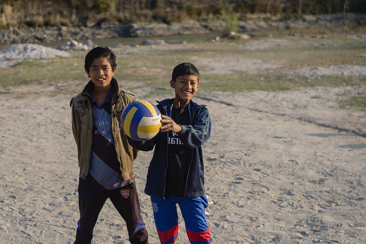 person smiling and standing boy holding volleyball beside standing boy sphere