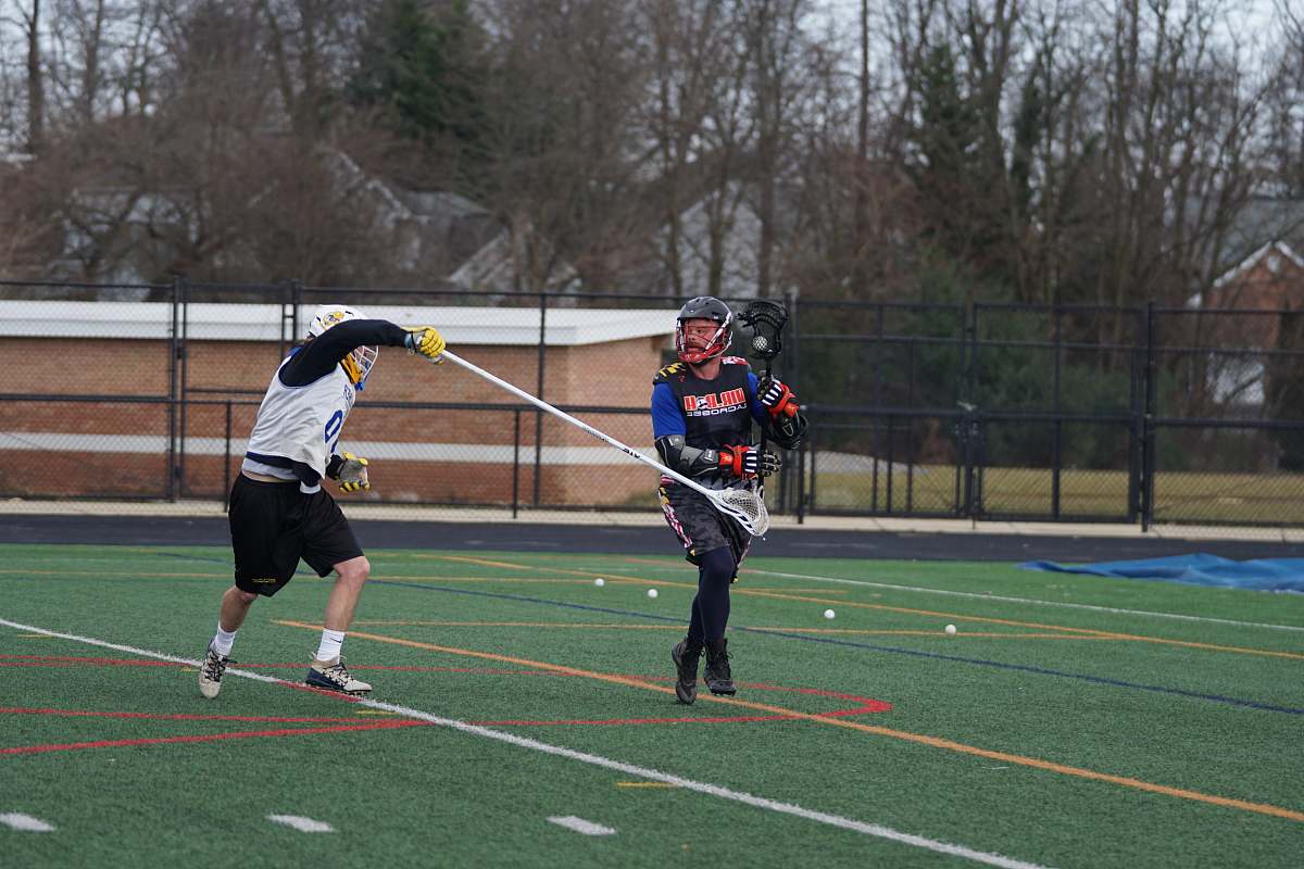 person two men playing lacrosse on green field field