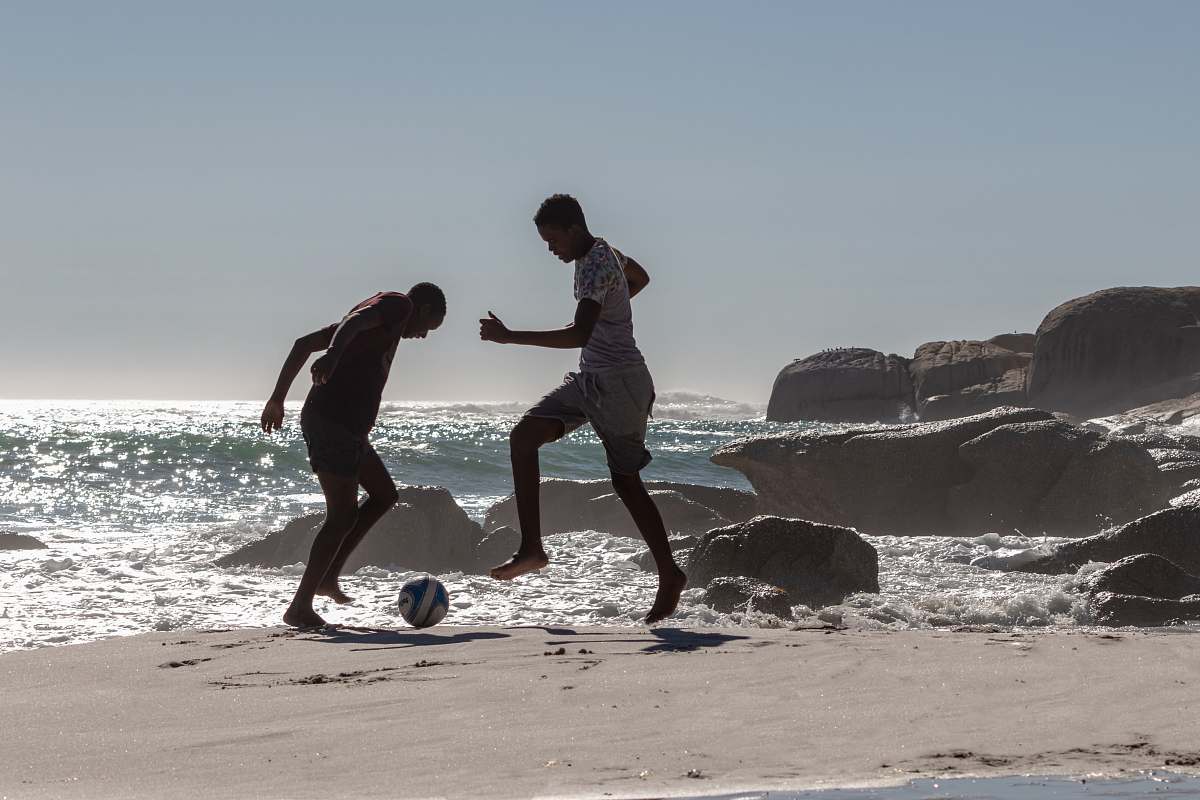 person two men playing with soccer ball near seashore soccer