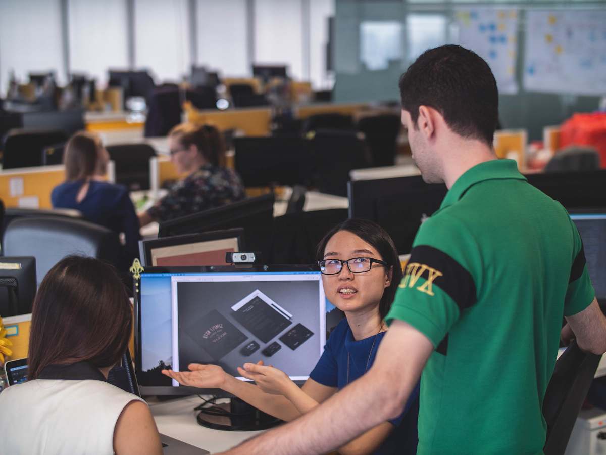 person woman sitting in front of computer monitor explaining something two man and woman beside her people