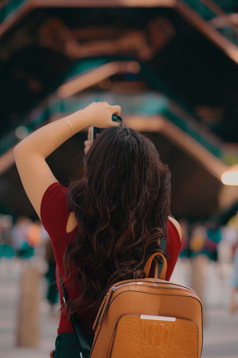 In this vibrant urban setting, a woman with a backpack is seen using her camera near an architectural marvel, capturing the essence of city life. The bustling train station serves as a backdrop, highlighting a perfect blend of adventure and exploration. This image is ideal for travel blogs, city guides, and content focusing on photography, urban exploration, and the spirit of adventure.