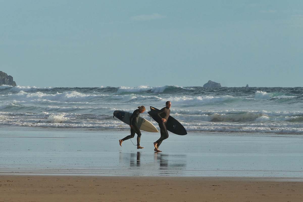 water man and woman holding surfboards running near seashore under blue and white skies during daytime nature