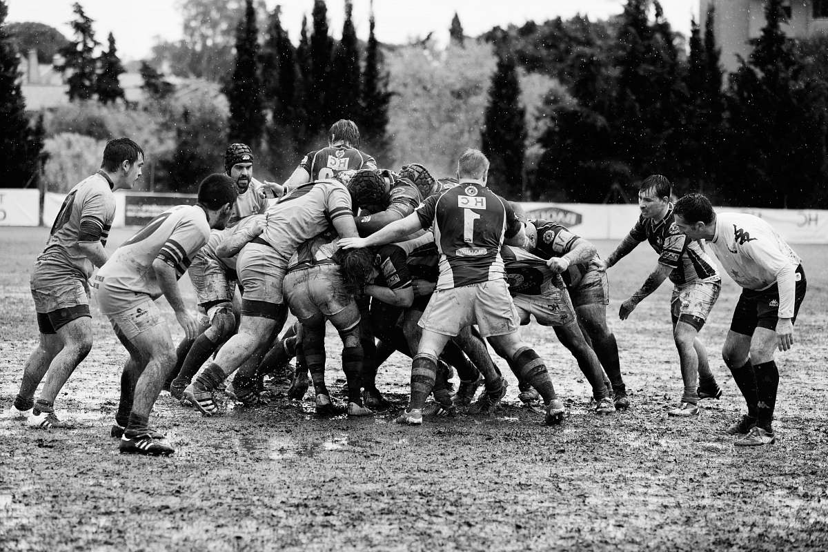 black-and-white grayscale photography of men playing rugby on muddy land sport