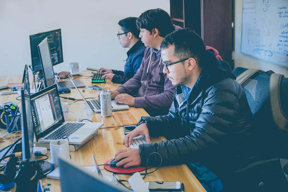 person three men facing computer monitors human